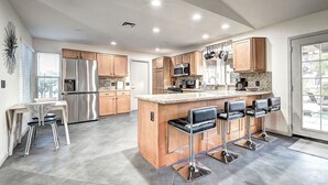 A modern kitchen with stainless steel appliances, wooden cabinets, a central island with bar stools, and a large window providing natural light. - Mesa Lake Front House With Pool and Hot Tub! (Mesa)