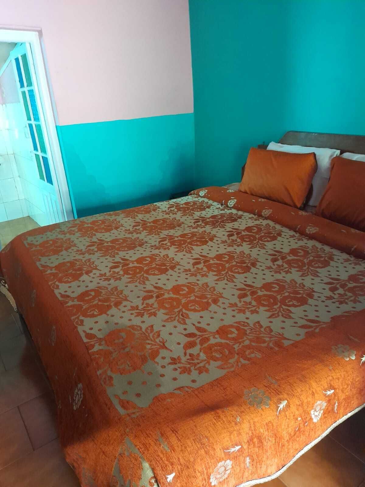 A bedroom with a bed, orange and white patterned bedspread, and a teal wall.