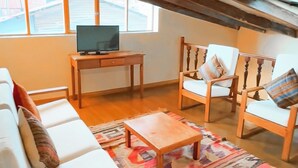 Un salon confortable avec un canapé, des fauteuils, une table basse et un téléviseur posé sur un meuble en bois.