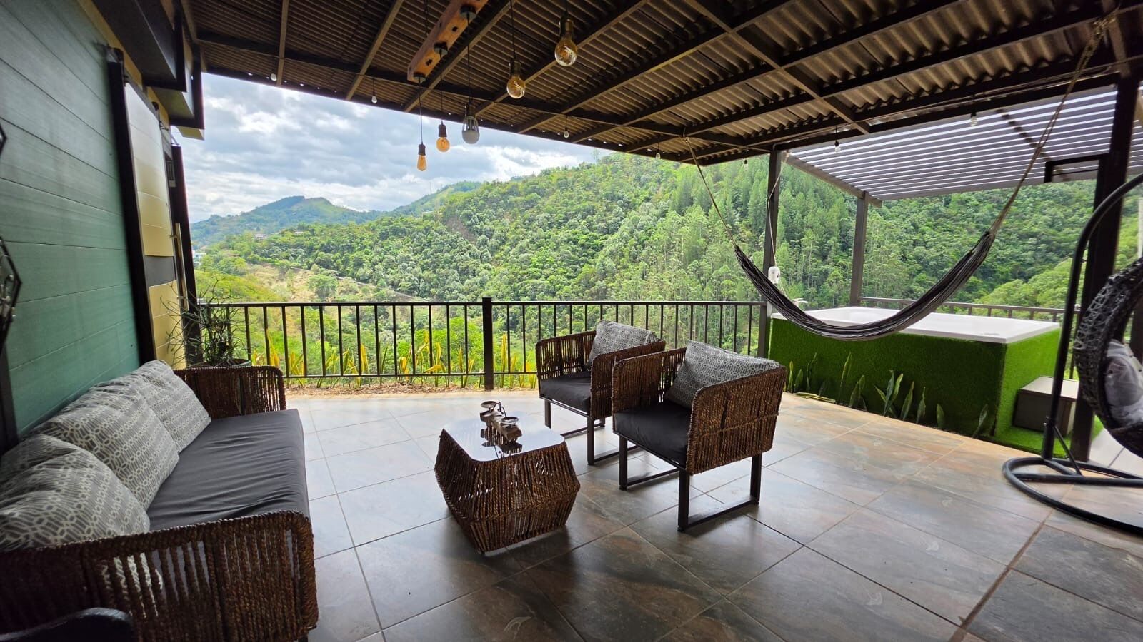 Un balcón con mobiliario de mimbre, una hamaca y vista a un paisaje verde exuberante.