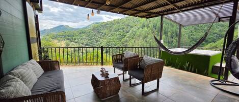 Un balcón con mobiliario de mimbre, una hamaca y vista a un paisaje verde exuberante.
