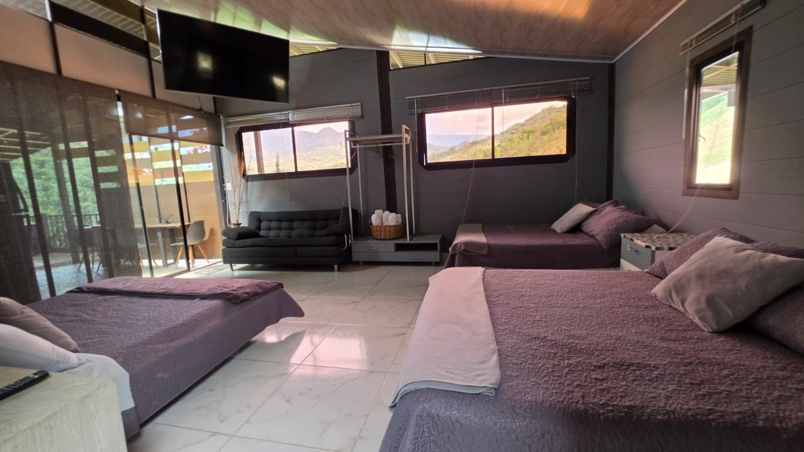 Ein Zimmer mit zwei Betten, einem Schlafsofa, einem Fernseher und einem Fenster mit Blick auf eine Berglandschaft.
