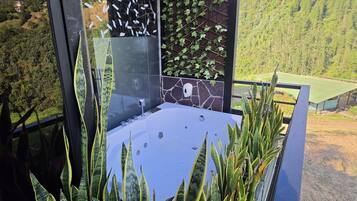 Un bagno moderno con cabina doccia in vetro, una vasca da bagno e vista su un paesaggio verde e rigoglioso.
