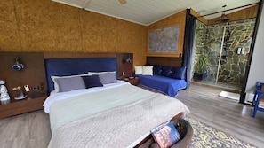 A bedroom with a large bed, a smaller sofa, a map on the wall, and a stone wall with a glass door.
