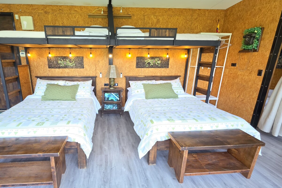 Ein Zimmer mit zwei Betten, einem Hochlaggerl, Holzboden und einem kleinen Nachttisch mit Lampe.