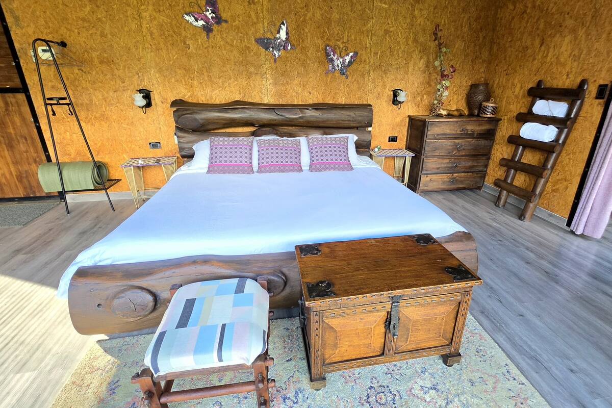 Une chambre avec une tête de lit en bois, un lit agrémenté d’oreillers à motifs, une table de chevet, une commode en bois, une échelle et des lampes fixées au mur.