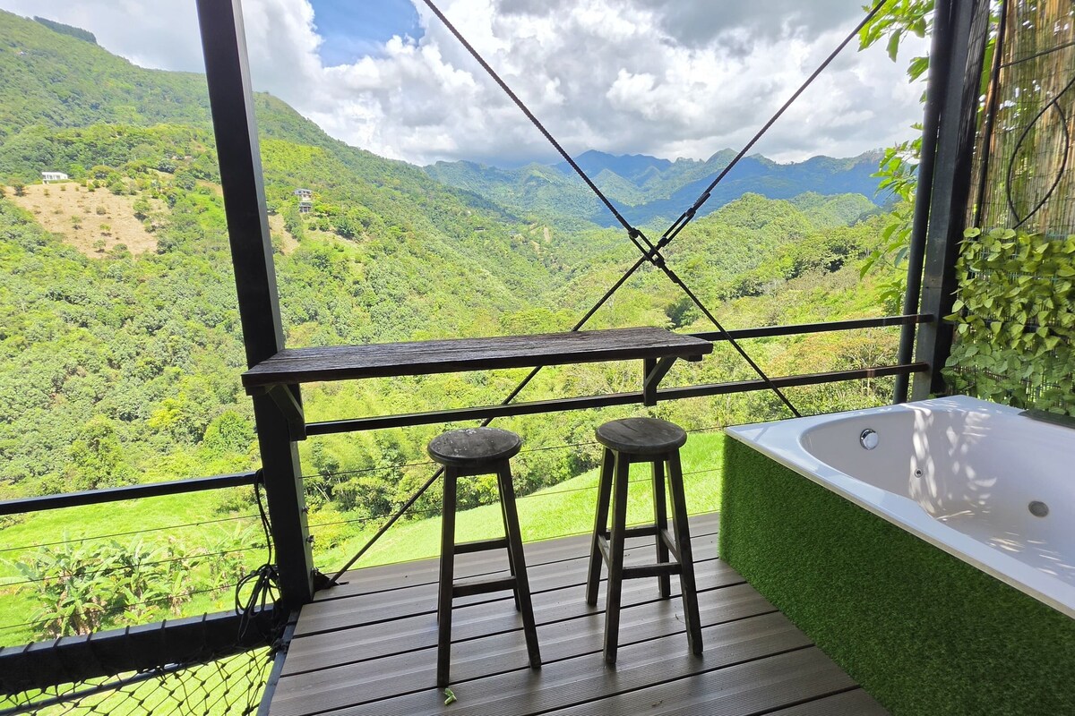 Ein Balkon mit Blick auf ein üppiges Tal, eine weiße Badewanne und zwei Hocker.