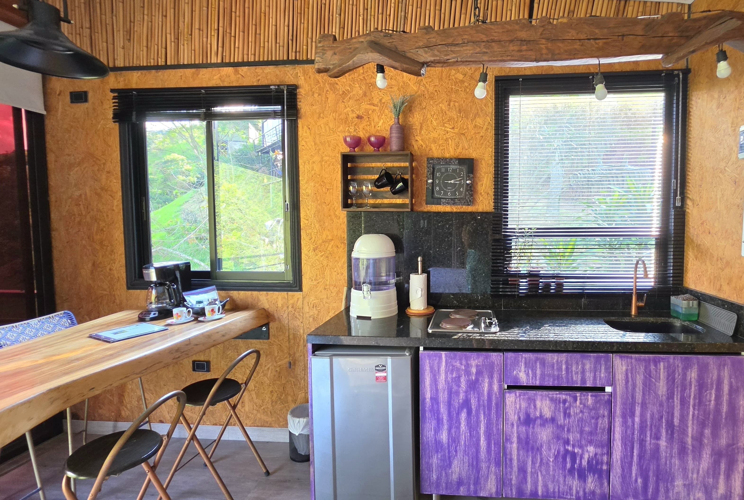 A compact kitchen with a wooden table, chairs, a refrigerator, and a sink.