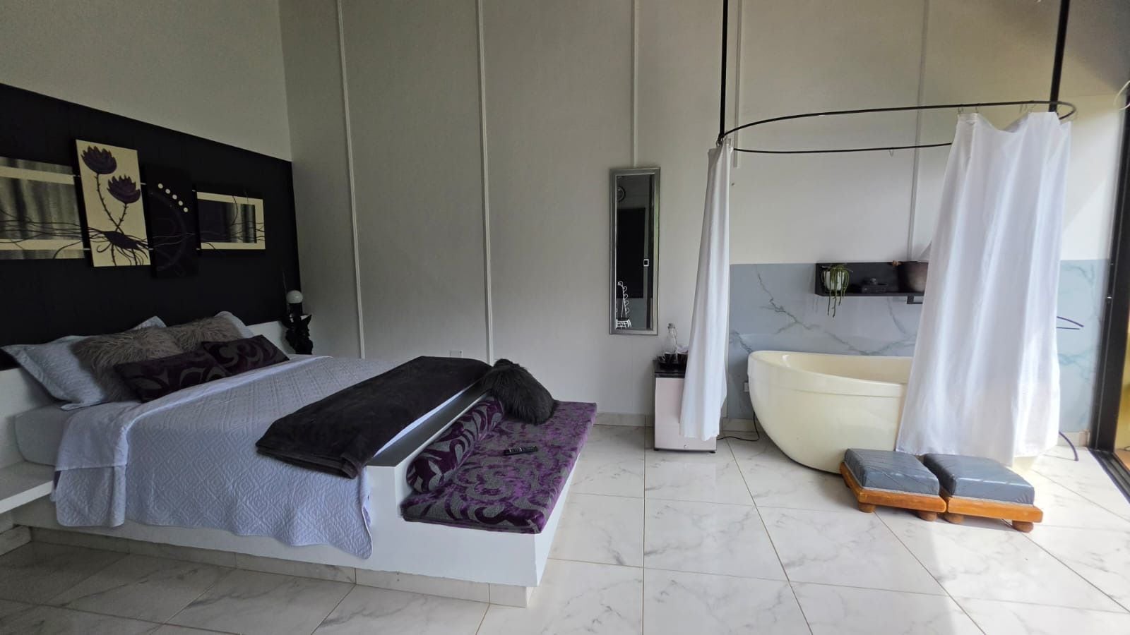 Un dormitorio moderno con una cama grande, una zona de estar separada, una bañera y una cortina de ducha.