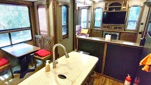 A compact kitchen with a sink, a window, and a small table with a red cushion.