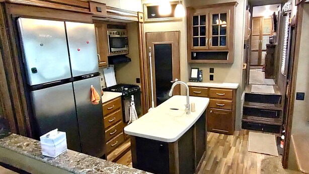 A compact kitchen with a refrigerator, stove, sink, and wooden cabinets.