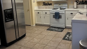 Una cocina con armarios blancos, un refrigerador de acero inoxidable, un microondas y una estufa. Hay dos felpudos en el suelo.