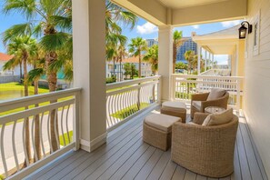 Un porche techado con muebles de mimbre y vistas a palmeras y edificios.