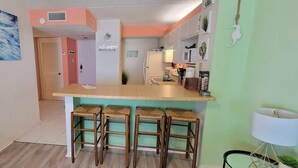 A kitchen with a wooden bar counter and stools, a refrigerator, and a sink.