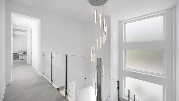 Een modern interieur met glazen balustrade, een plafondlamp en zicht op een andere kamer.