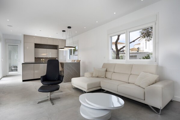 A modern living room with a sectional sofa, a black chair, a white coffee table, and a kitchen in the background.