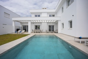 A modern pool area with a rectangular pool, lounge chairs, and a covered seating area.
