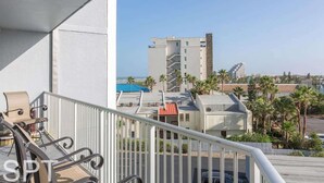 Un balcón con vista a un conjunto de edificios, que incluye una estructura alta de diseño único y un edificio más pequeño con techo rojo.