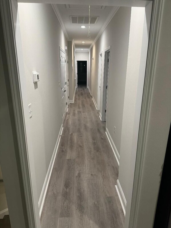 Un pasillo largo y estrecho con suelo de madera y paredes blancas.