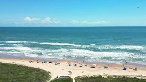 A beach with people, umbrellas, and a lifeguard tower. - High Floor 3BR Corner, Beachfront Saida Towers SPI (South Padre Island)