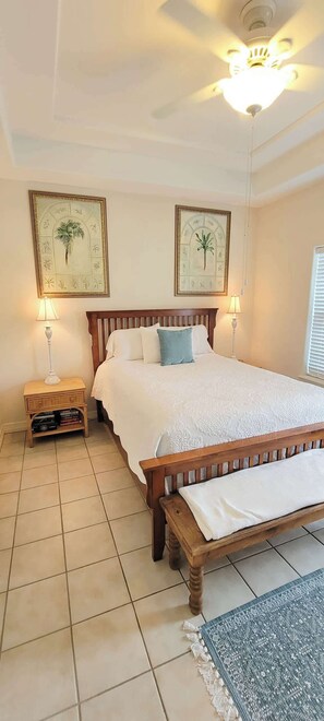 A bedroom with a bed, two wall-mounted lamps, a ceiling fan, and two framed botanical prints on the wall.