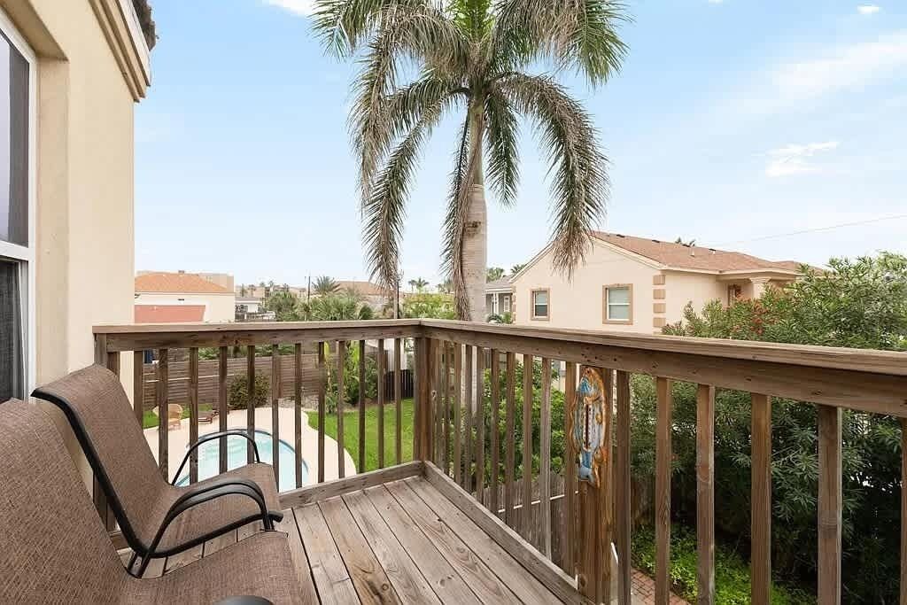 A balcony with wooden railings, a pool, and a palm tree.