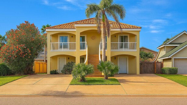 A two-story residential building with a central entrance, a balcony on the second floor, and a palm tree in front.