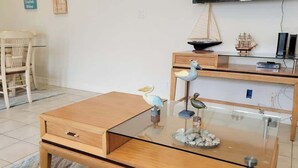 A modern living room with a glass-top coffee table, a wooden side table, and a small ship model on a shelf.