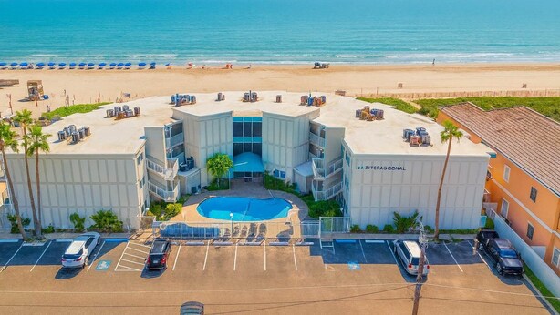 A hotel with a central pool, parking, and a beach view.