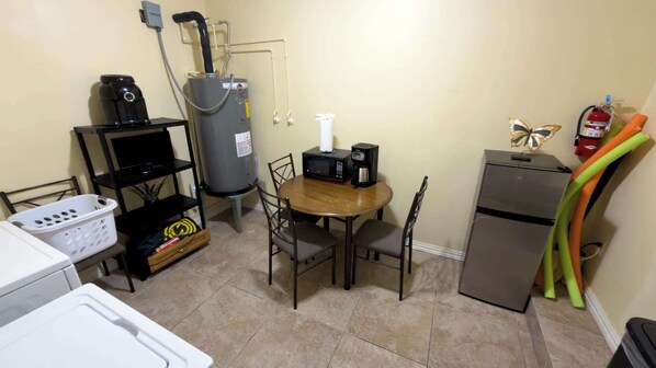 Une cuisine compacte comprenant une table, des chaises, un réfrigérateur, un four à micro-ondes, une machine à café, un chauffe-eau et un extincteur.