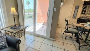 Ein Wohnzimmer mit Sofa, einem kleinen Tisch mit Lampe, einem Balkon mit Stuhl und einem Essbereich mit Stühlen und Tisch.