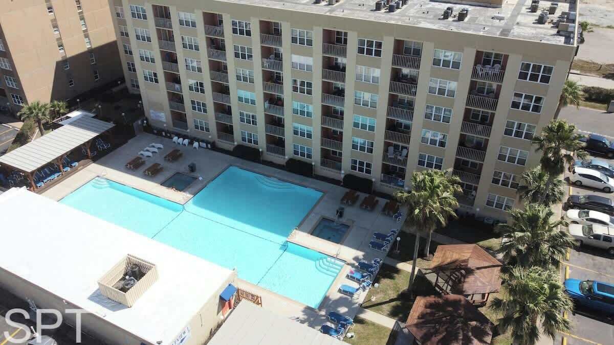 Un hotel con un amplio área de piscina, varios balcones y un estacionamiento.