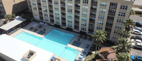 Un hotel con un amplio área de piscina, varios balcones y un estacionamiento.