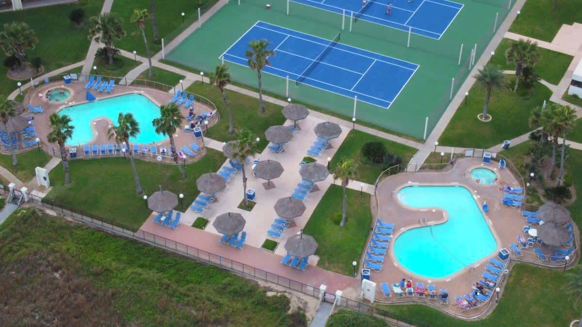 Een luchtbeeld van een resort met twee zwembaden, tennisbanen en ligbedden.