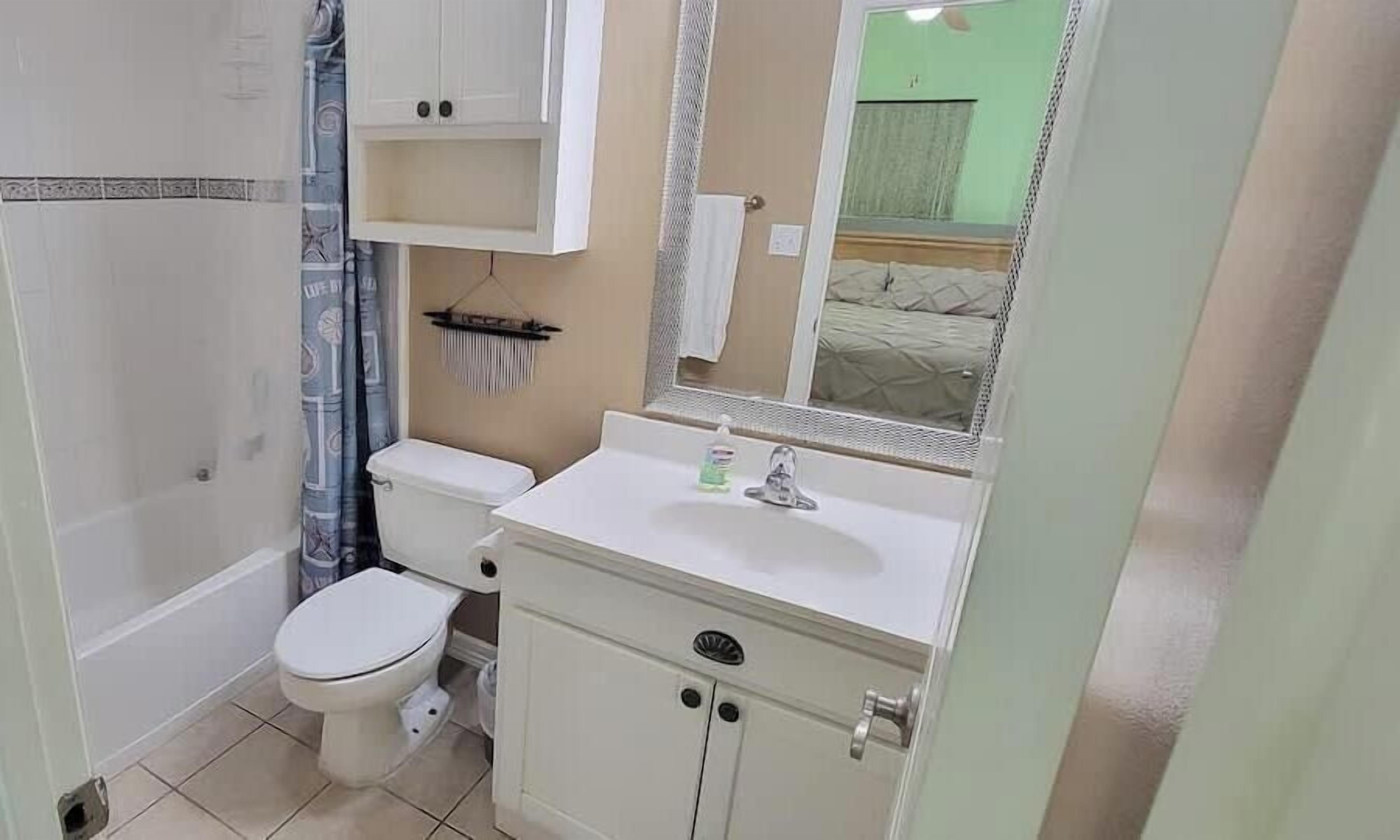 A bathroom with a toilet, sink, mirror, and a shower area.