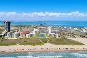 A coastal resort with multiple hotel buildings, a beach, and a bridge in the background. - 3BR 10th Floor Views, Beachfront Saida Towers SPI (South Padre Island)