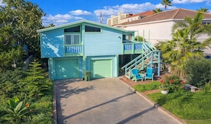 Une maison à deux étages, avec une façade bleue, un porche à l’avant orné de chaises bleues et un escalier menant à l’étage supérieur.