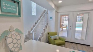 Una escalera que lleva a un segundo piso, una silla verde y una puerta con vista al exterior.