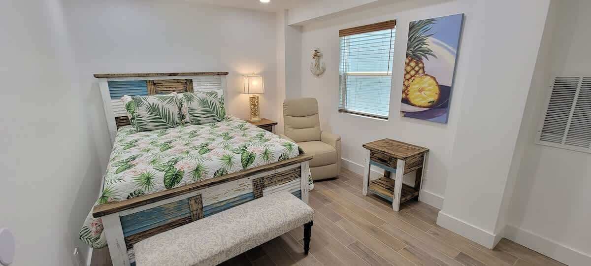 A bedroom with a bed, a chair, a small table, and a window with blinds.
