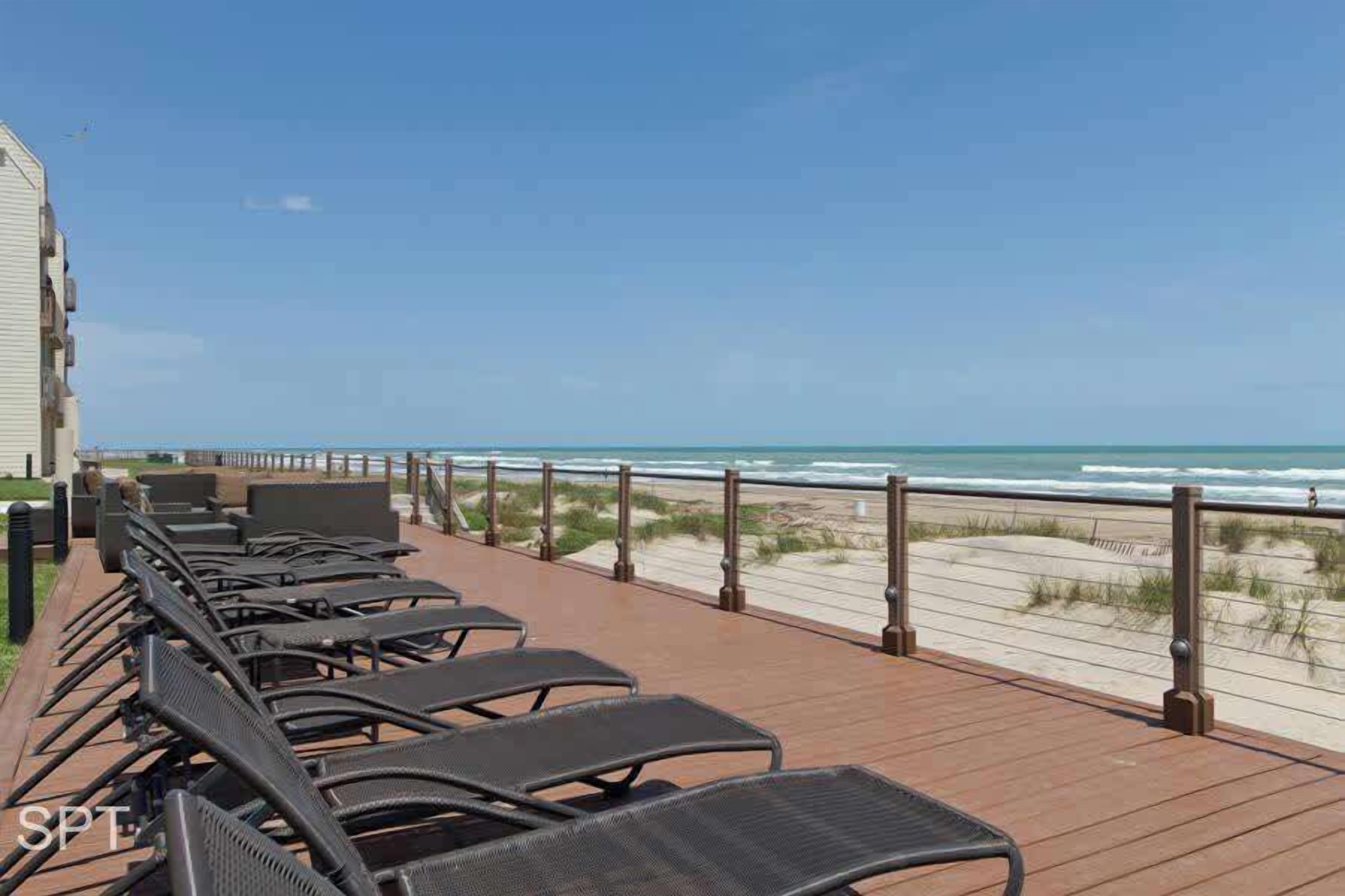 A wooden deck with outdoor seating, a beach view, and a building in the background.