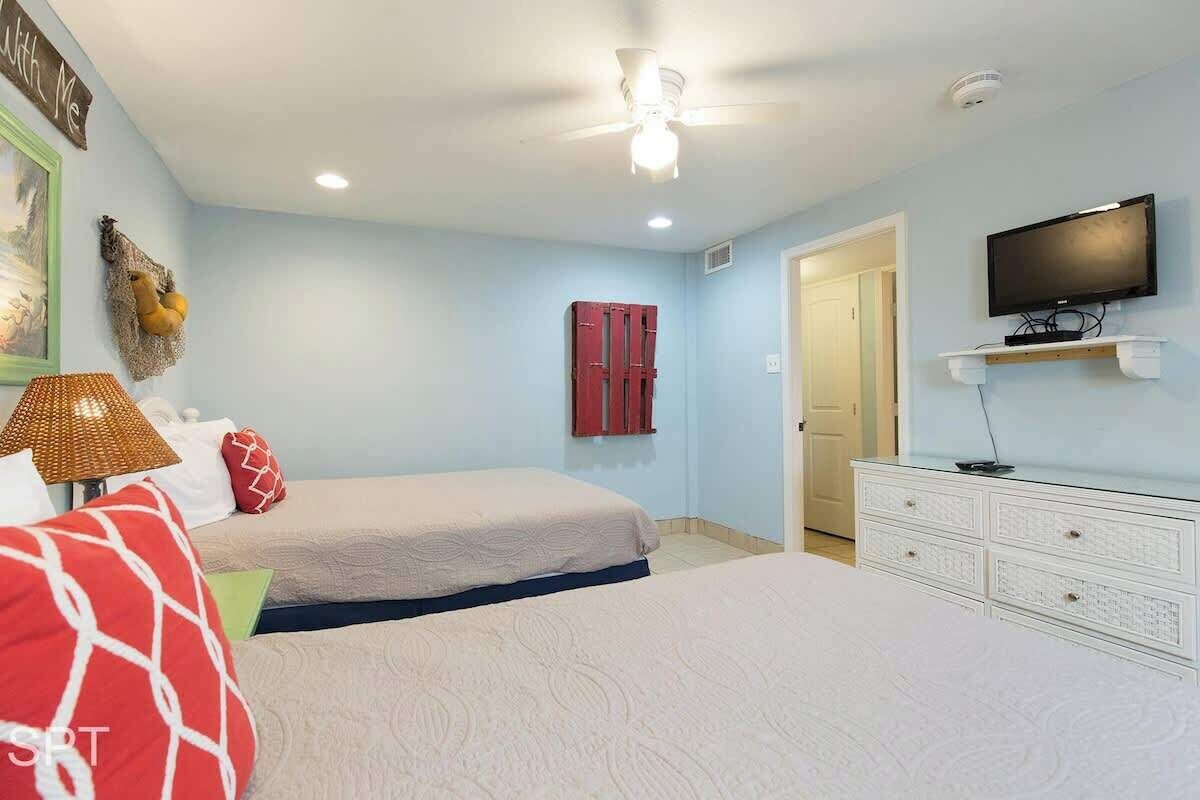 A bedroom with two beds, a ceiling fan, a television, and a dresser.