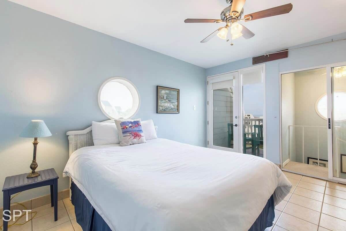 A bedroom with a bed, a ceiling fan, a nightstand, a window, and a door leading to a balcony.