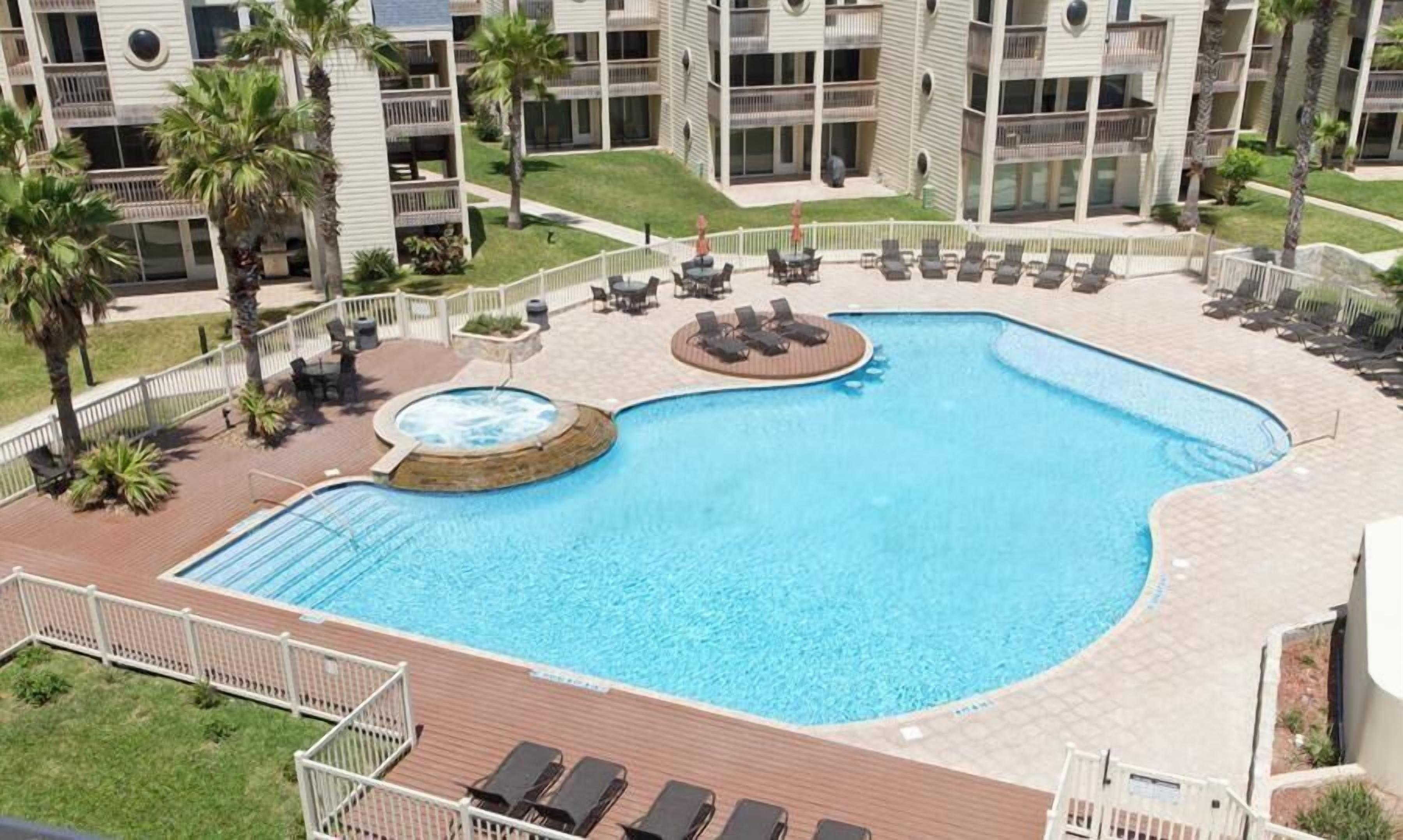 Piscina con jacuzzi, rodeada de sillas de descanso y palmeras.