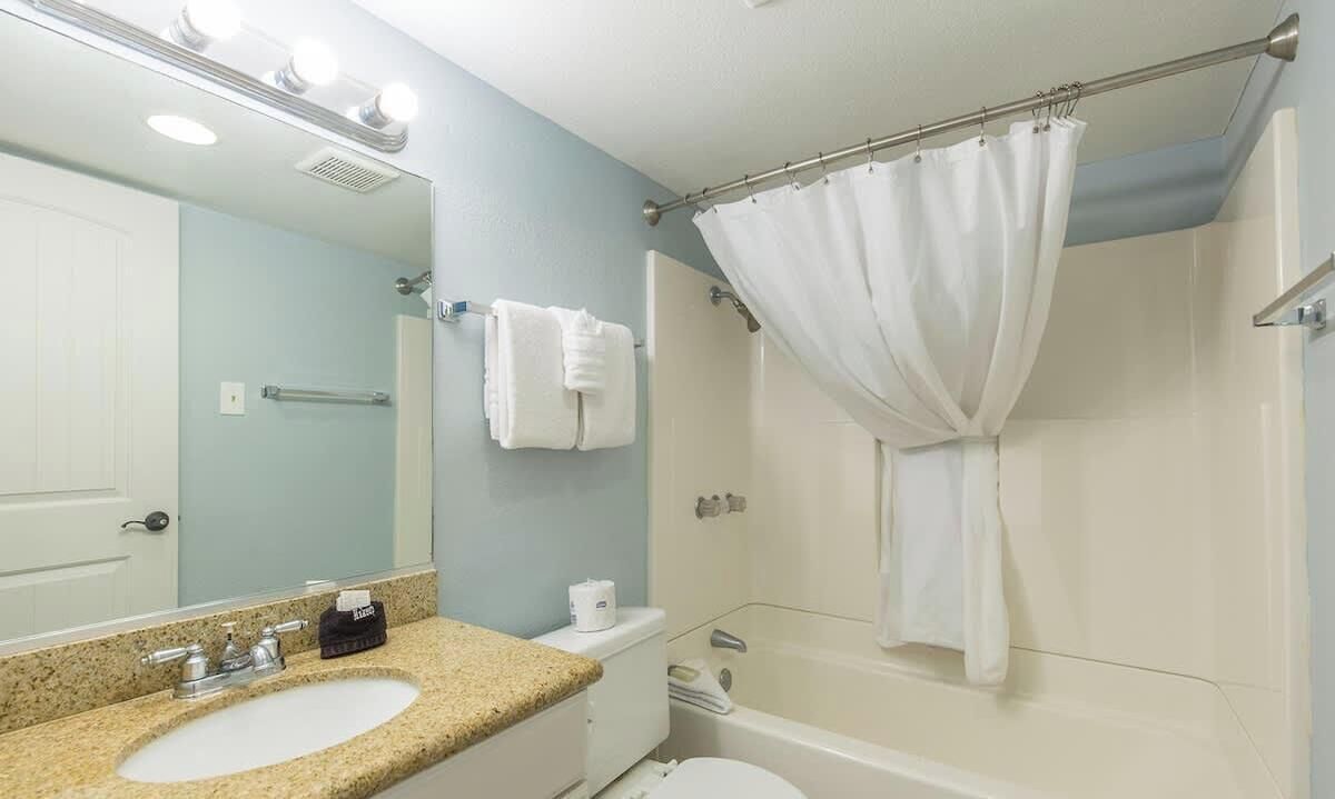 A bathroom with a sink, mirror, shower, and toilet.