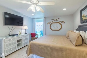 Ein Schlafzimmer mit einem Bett, einem Fernseher, einem Deckenventilator, einer Kommode und einem Fenster.
