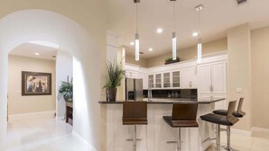 A modern kitchen with three bar stools, white cabinetry, and pendant lighting. - Big Private Luxury Home in Beach Gated Community (South Padre Island)