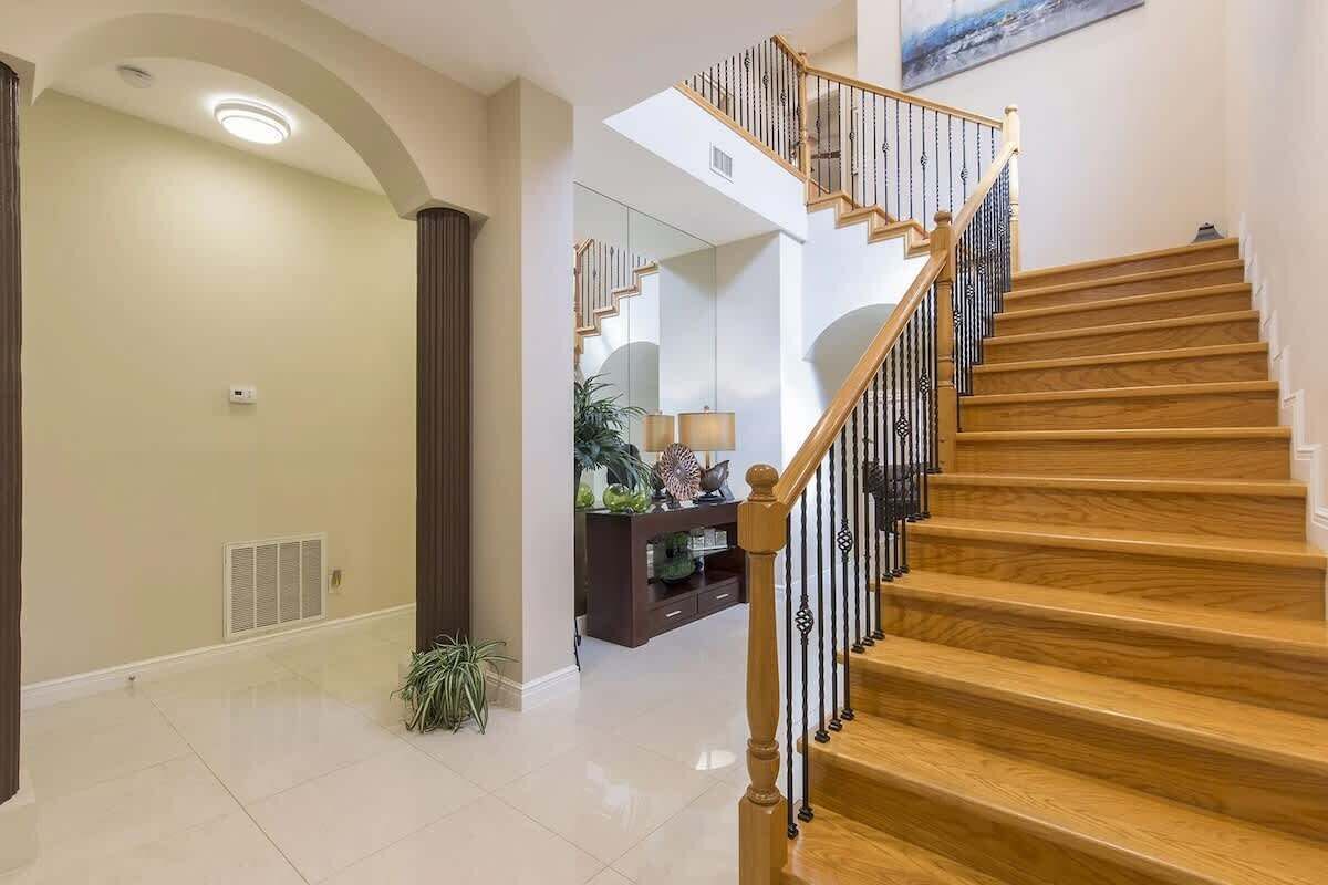 A modern interior with a wooden staircase, a hallway leading to a living area, and a large mirror reflecting the space.