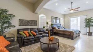 A spacious living room with a black leather sofa, a round coffee table, and a large bed in the background. - Big Private Luxury Home in Beach Gated Community (South Padre Island)