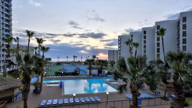 Ein Hotelpoolbereich mit Liegestühlen, Palmen und Blick auf den Sonnenuntergang.
