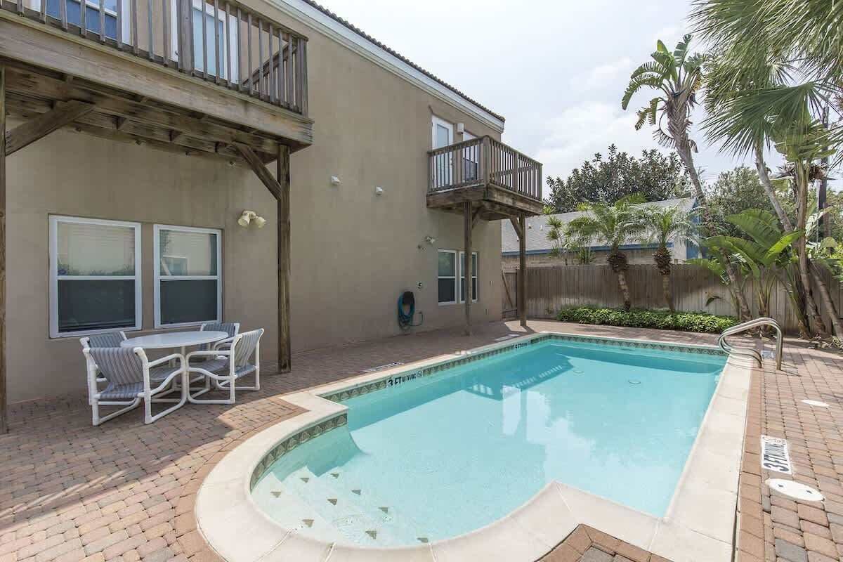 A backyard with a swimming pool, a patio table with chairs, and a wooden deck.